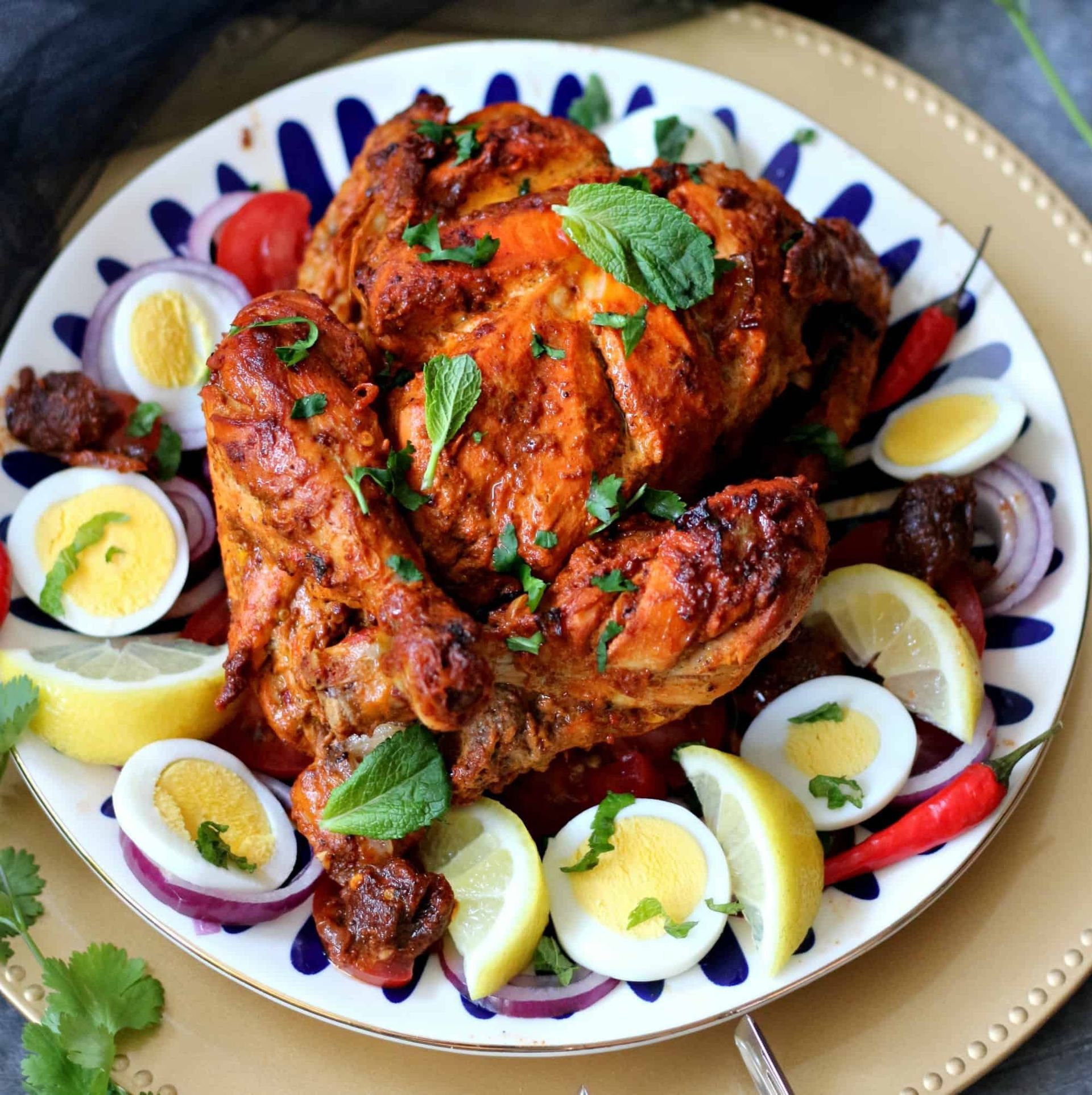 Roasted spiced chicken on a plate, garnished with basil and surrounded by halved boiled eggs and onions