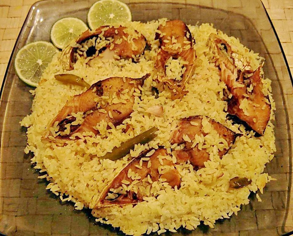 Platter of rice topped with grilled fish and lemon slices on a glass dish