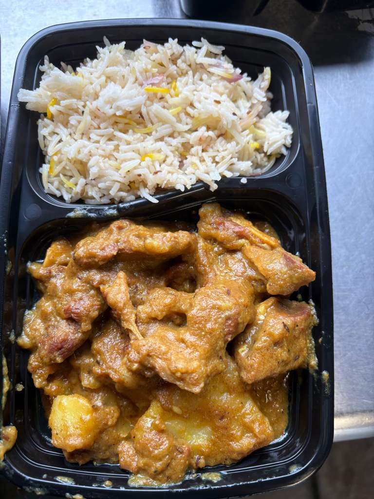 Takeout tray with rice and saucy chicken wings on a black plastic container