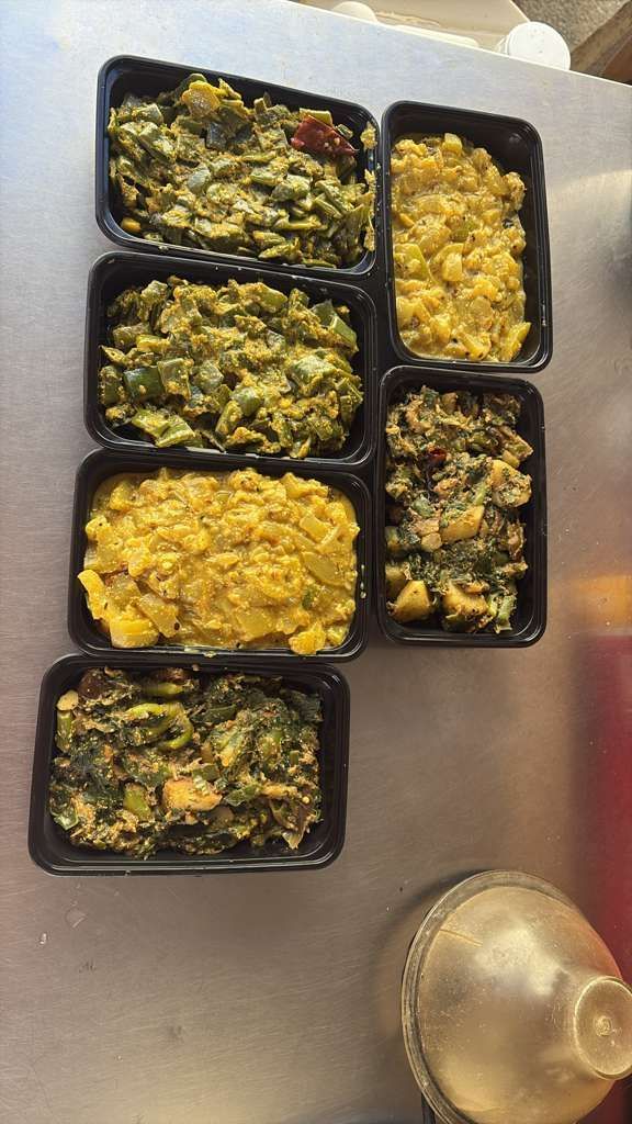 Meal prep containers with assorted cooked vegetables on a stainless steel counter.