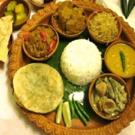 Traditional Indian thali with rice, curries, flatbread, chutney, and sliced vegetables on a carved platter