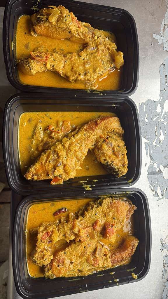 Three black meal containers with yellow sauced chicken pieces on a white countertop.