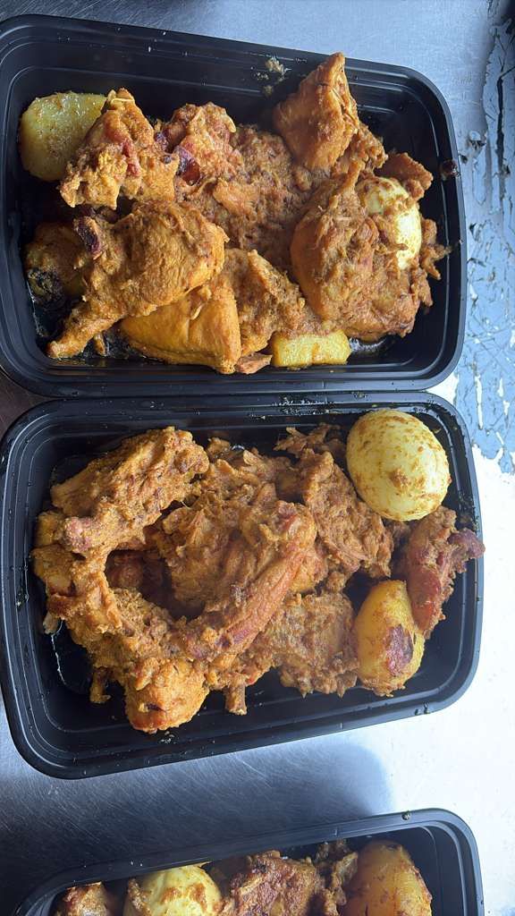 Three black meal containers with seasoned fried chicken and potato pieces on a dark countertop