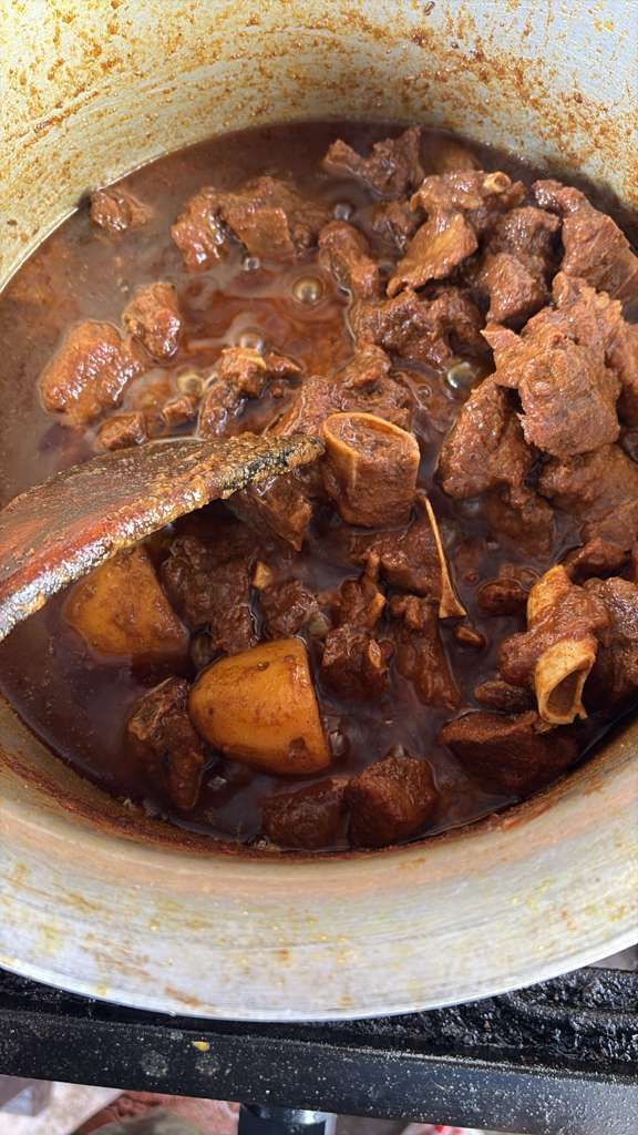 Chunks of meat simmering in a dark brown stew in a pot with a wooden spoon