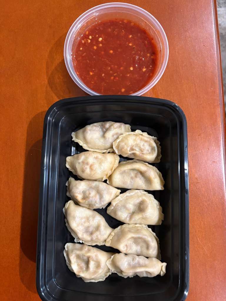 Container of dumplings with a cup of red dipping sauce on a wooden table