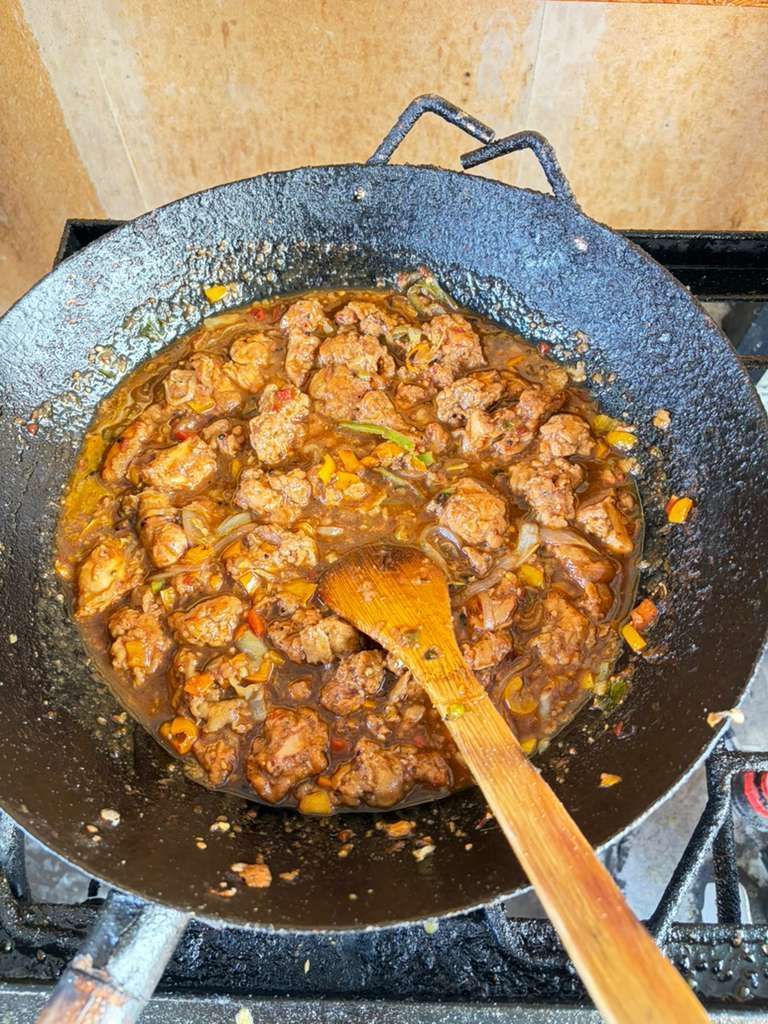 Spiced meat simmering in a black wok, stirred with a wooden spatula on a stovetop.