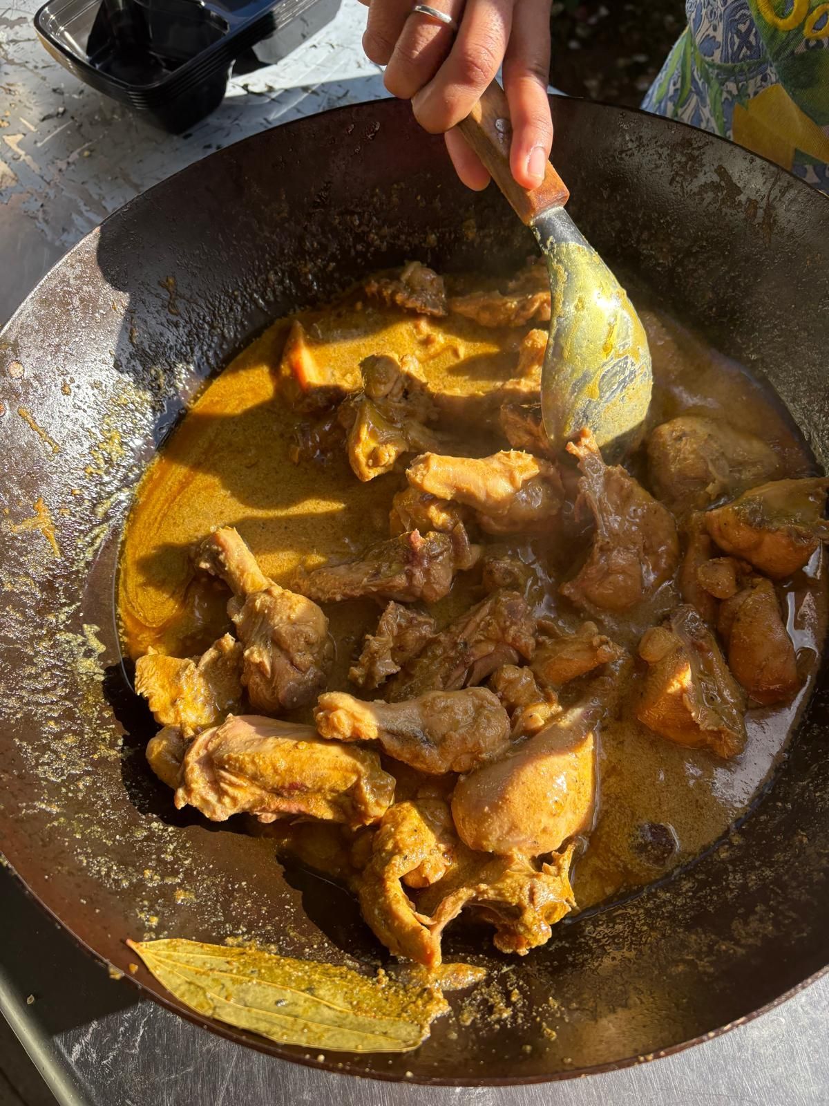 Person stirring chicken curry in a wok with a spoon