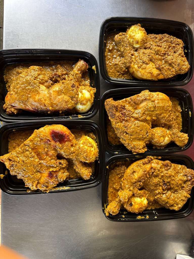 Five black meal containers with seasoned cooked chicken pieces on a metal surface.