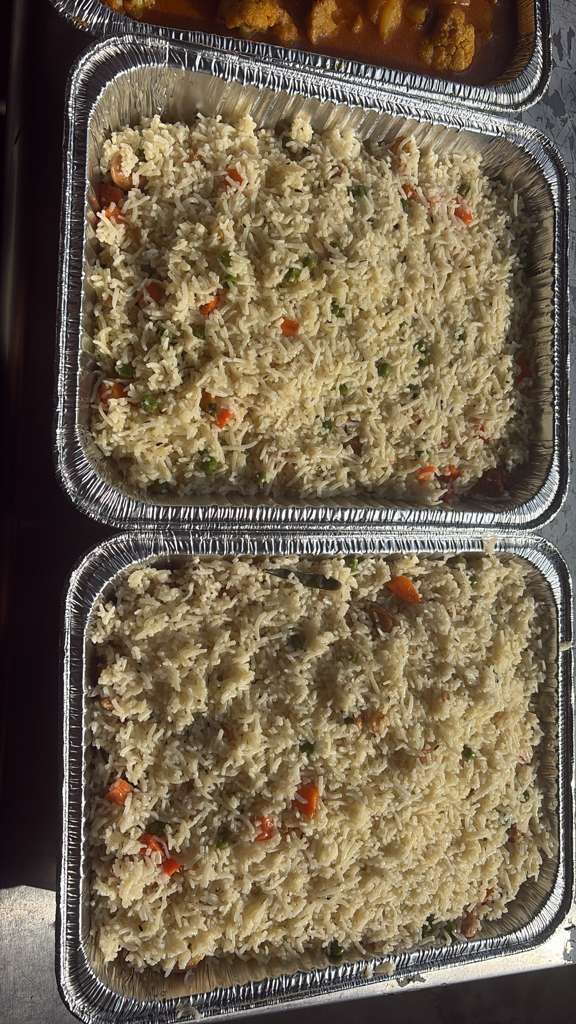 Two foil pans of rice and vegetable casserole, topped with baked crumbs and red pepper bits.