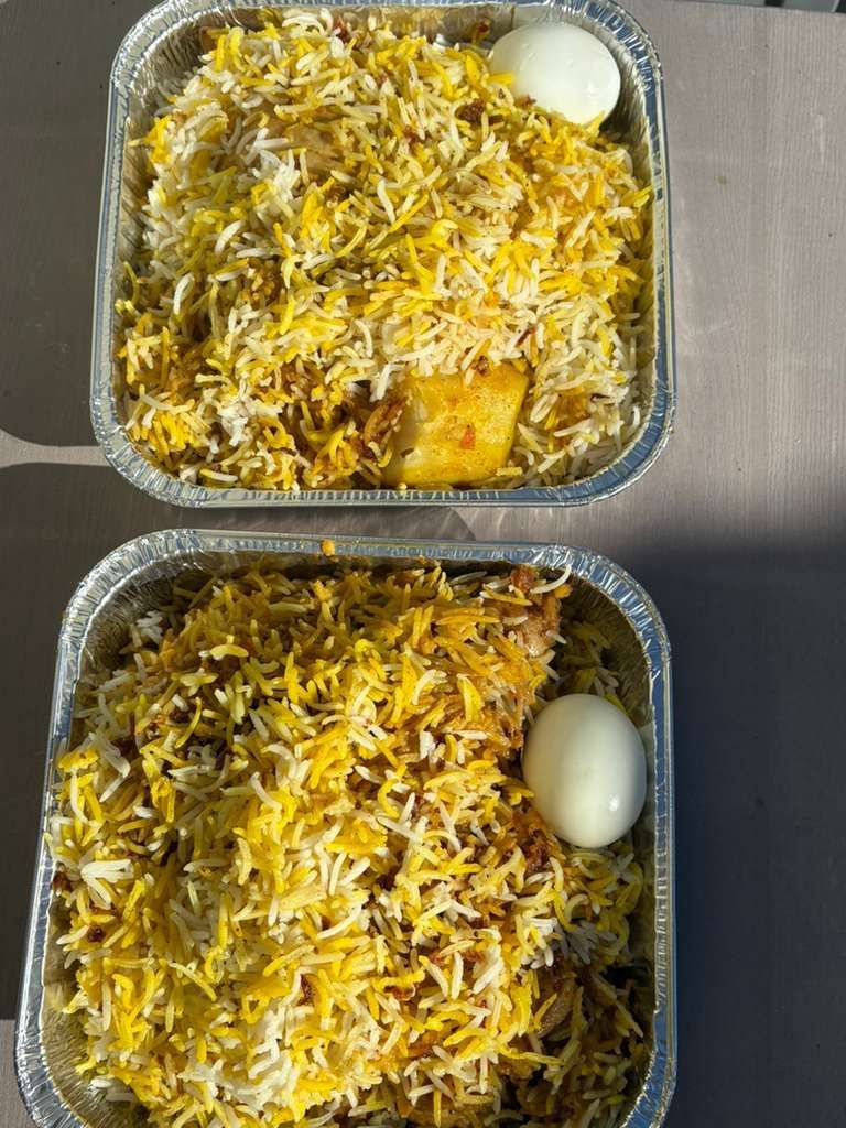 Two foil meal trays topped with yellow rice, shredded cheese, and a boiled egg each.