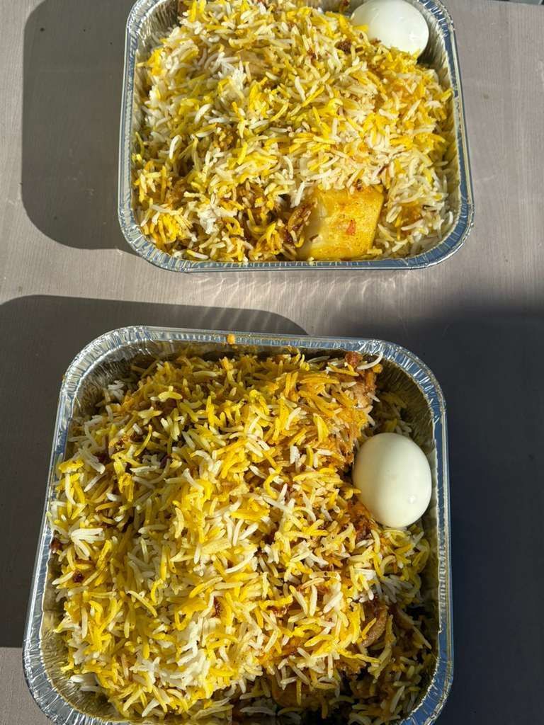 Two foil lunch trays of rice and chicken, each topped with shredded cheese and a boiled egg on the side