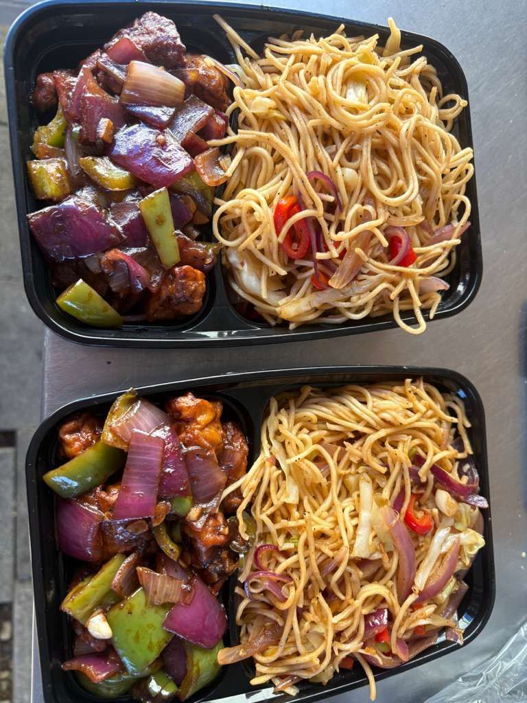 Two black meal trays with stir-fried veggies and noodles, including purple onions, peppers, and cabbage