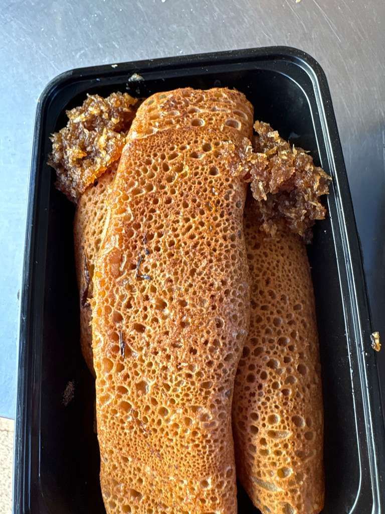 Two brown honeycomb-like rolled foods in a black takeout tray