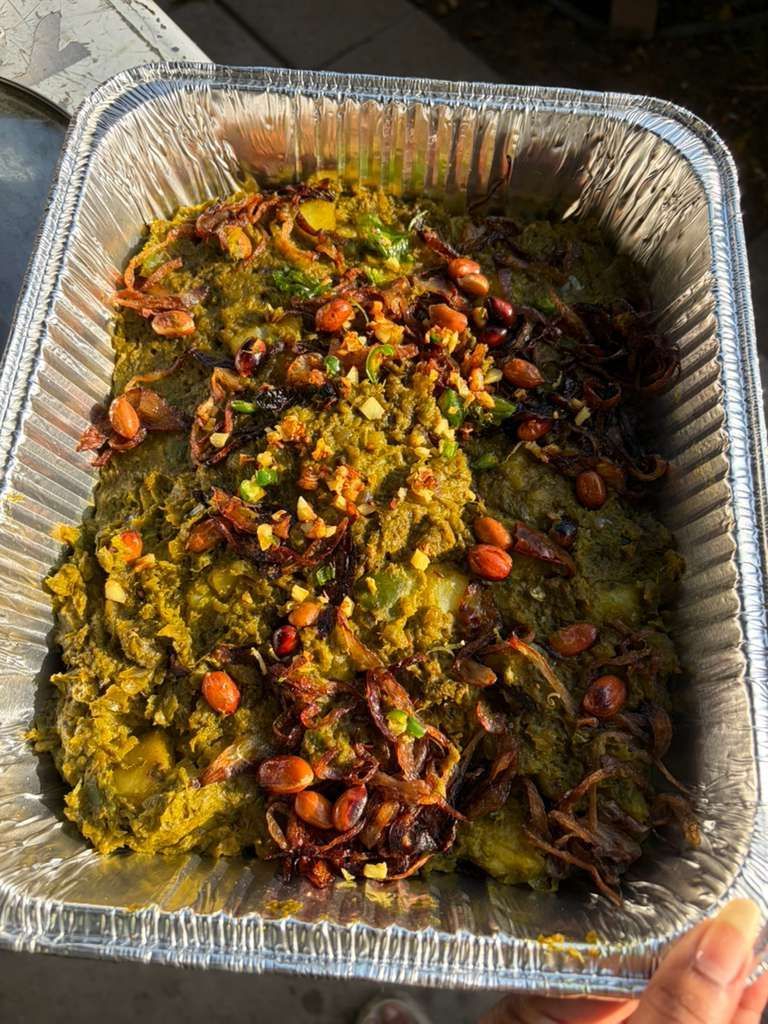 Foil tray of roasted vegetables topped with herbs and nuts, browned and colorful.