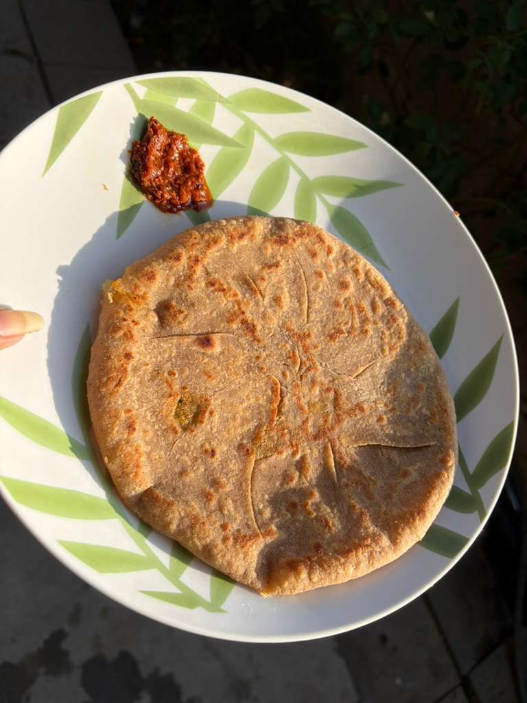 Plate with a browned flatbread and a small serving of red chutney on a white dish with green leaf pattern.