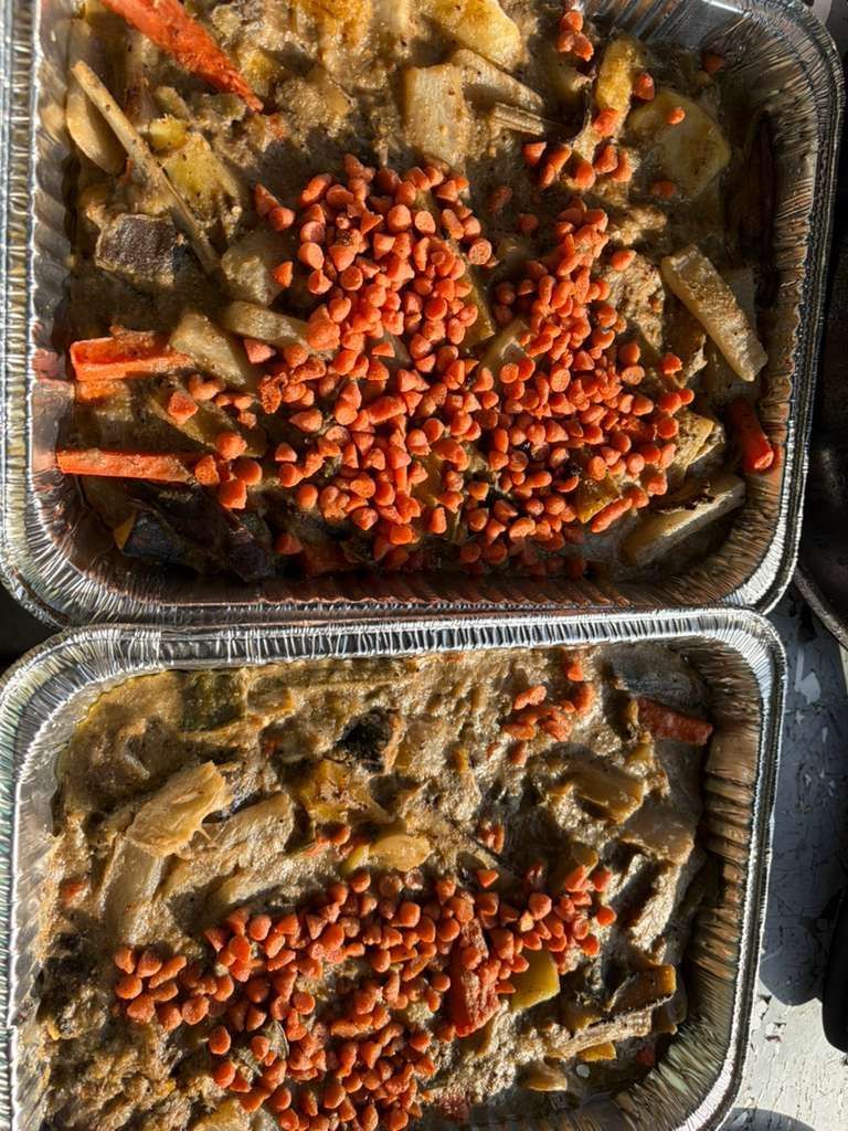 Two foil pans of cooked vegetables topped with red cherry tomatoes, viewed from above.