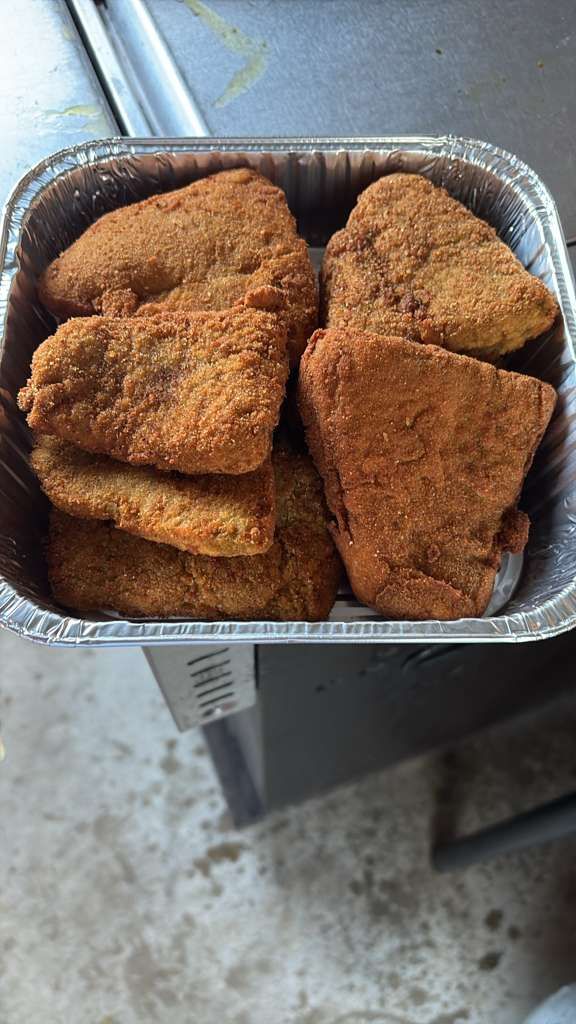 Container of breaded fried food pieces in a foil tray outdoors