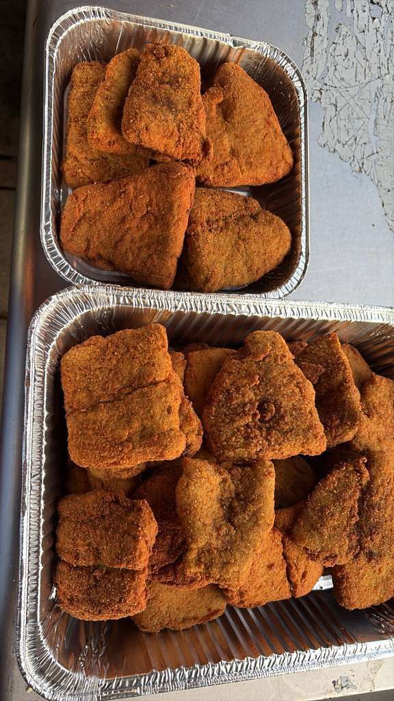 Two foil pans filled with golden-brown breaded chicken pieces on a countertop