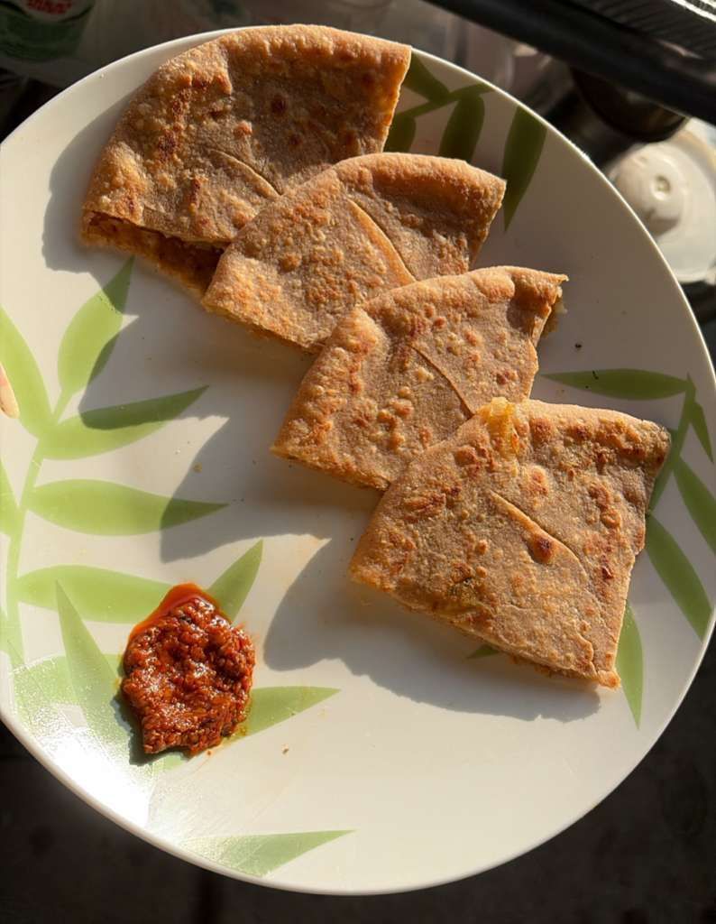 Plate with four folded flatbread pieces and a small dollop of red chutney on a leaf-patterned plate.