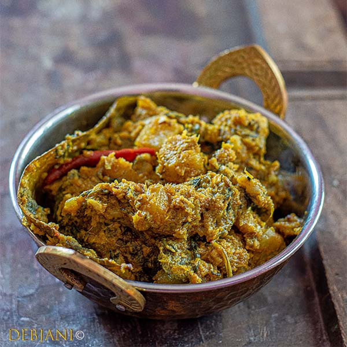 Copper bowl of creamy yellow curry with red chilies on a wooden table