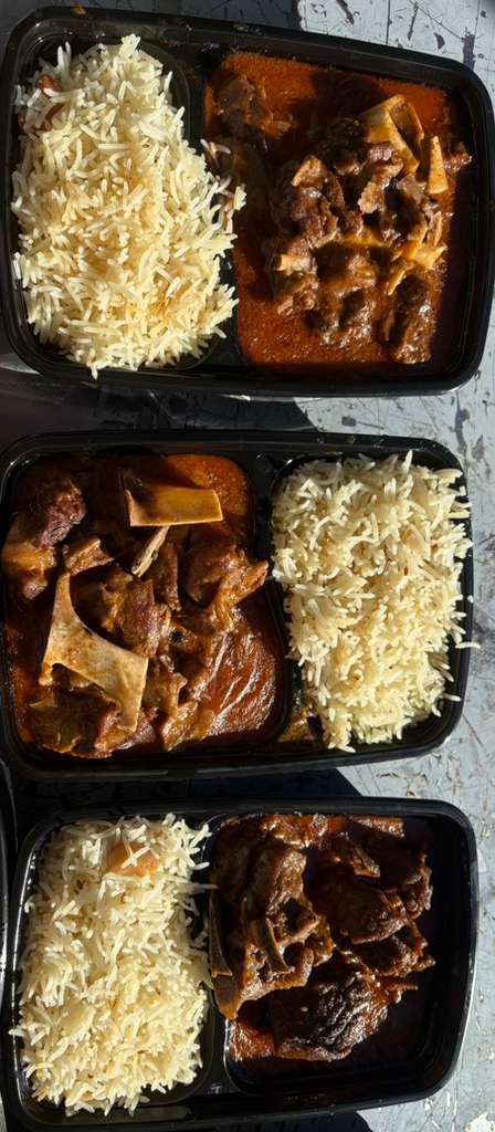 Three meal trays with rice and stewed meat in black takeout containers.