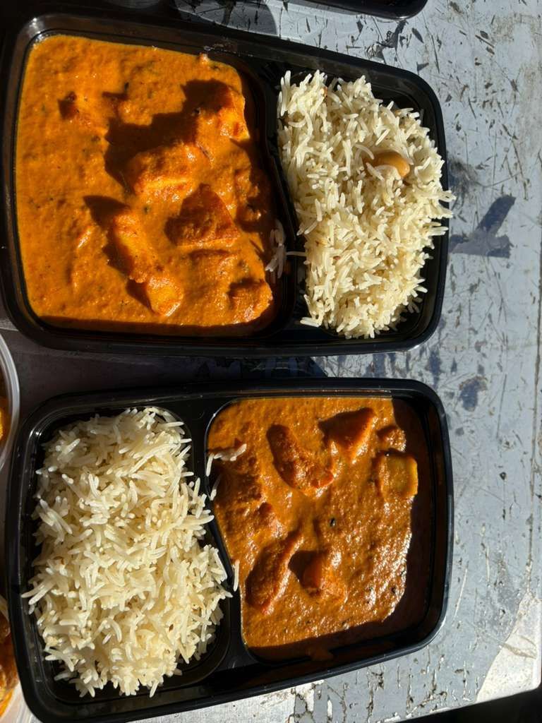 Two takeout trays with butter chicken and rice on a table