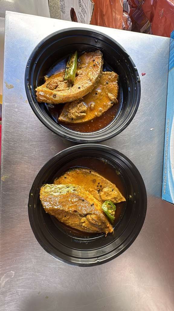 Two black bowls of fish curry on a metal tray, with orange sauce and fish pieces.