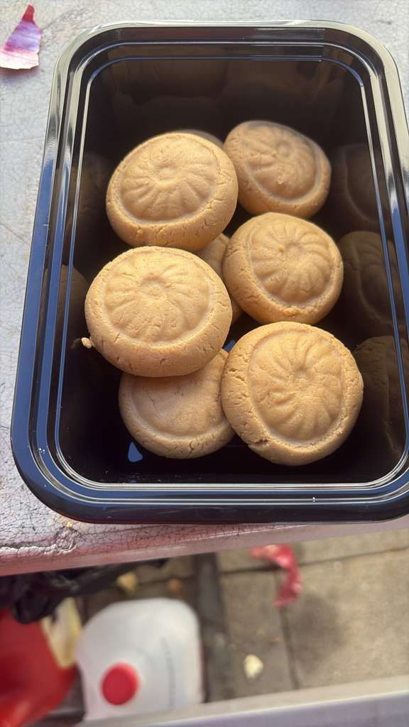 Black plastic container with six round beige cookies or biscuits on a patterned tablecloth.