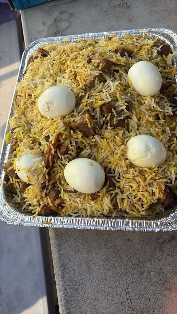 Tray of biryani topped with five boiled eggs on a concrete surface