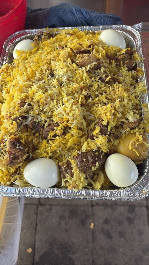 Foil tray of biryani topped with yellow rice and whole boiled eggs on a table