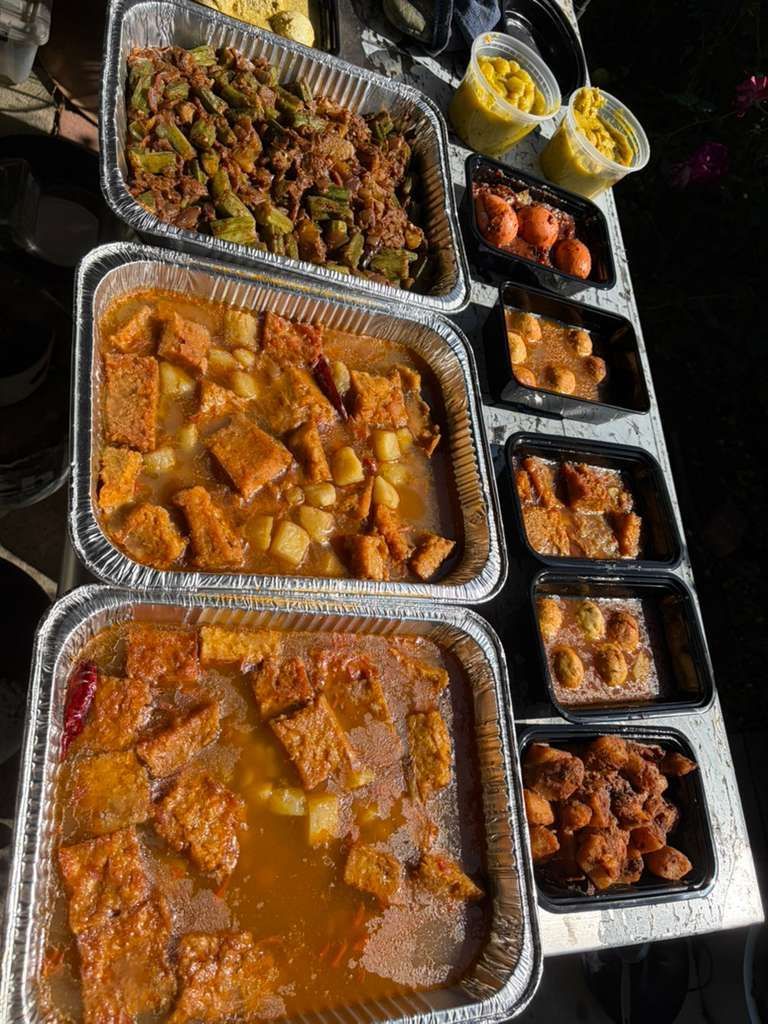 Takeout trays of assorted saucy dishes and sides arranged on a dark table.