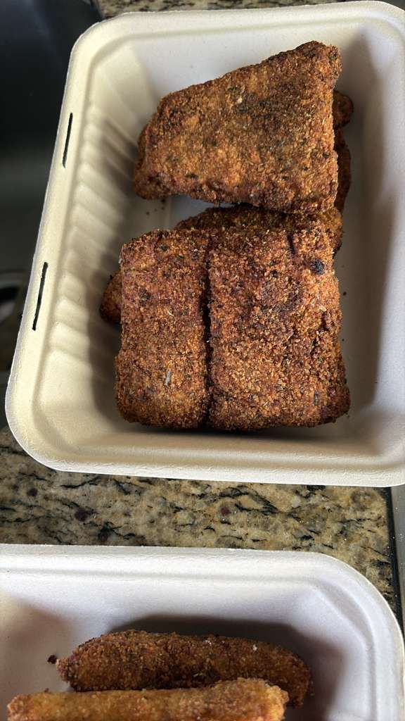 Two takeout containers holding browned, seasoned meat pieces on a countertop.