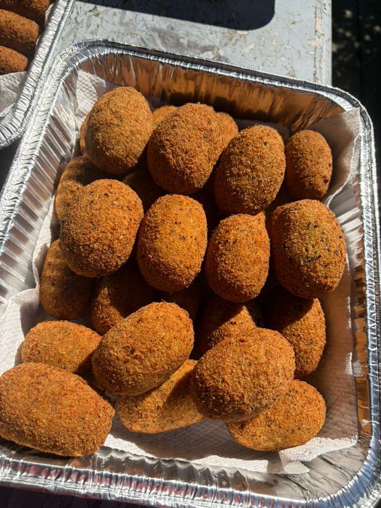 Tray of breaded fried snack bites in a foil pan on a table outdoors