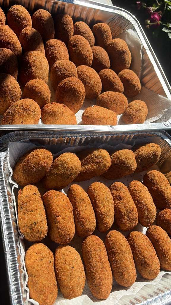 Trays of golden-brown breaded croquettes arranged in rows at a food display.