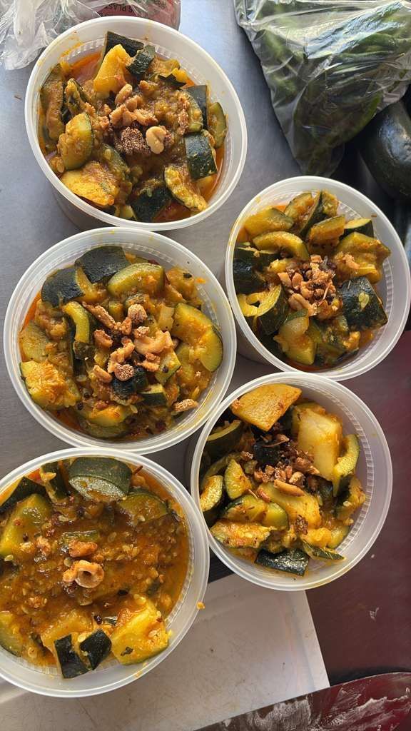 Five bowls of yellow-green vegetable curry or stew, arranged on a table with a plastic bag nearby