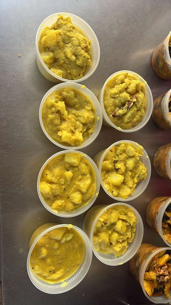Small white cups of yellow mashed food arranged on a table, with jars or containers along the right side.
