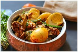 A bowl of spicy curry with eggs and meat, garnished with lemon slices and herbs
