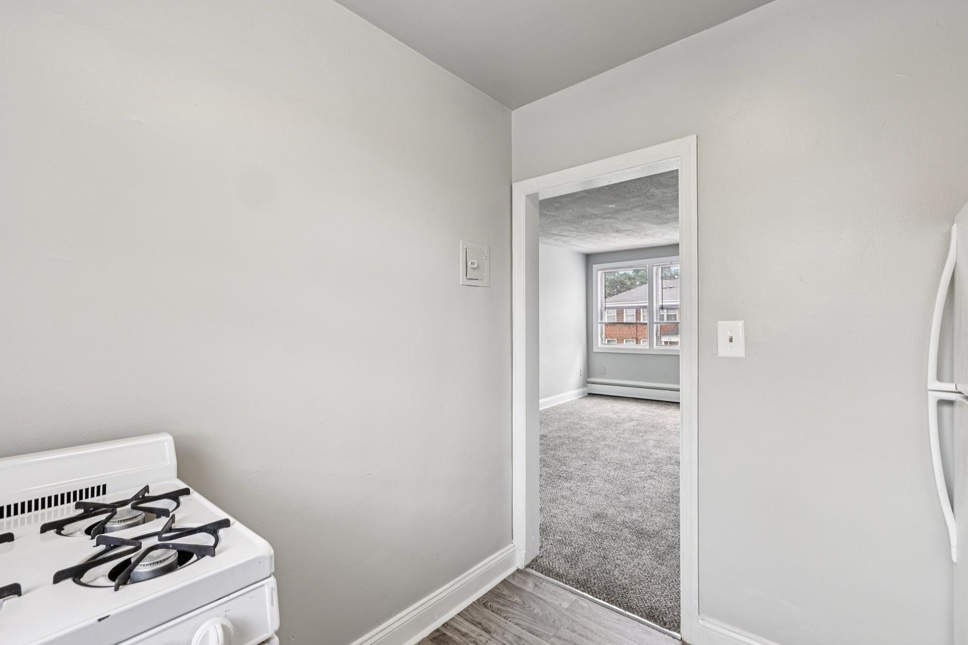 Kitchen with a stove and doorway leading to a carpeted room with a window. Gray walls.