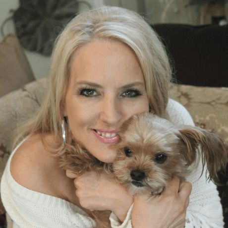Blonde woman smiling and hugging a small tan dog on a couch