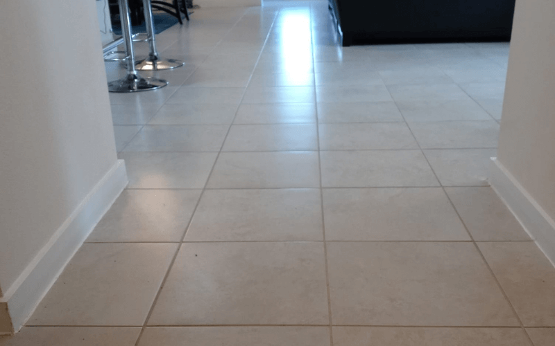 Hallway with light beige tiled floor, white walls, and bright light at the end.