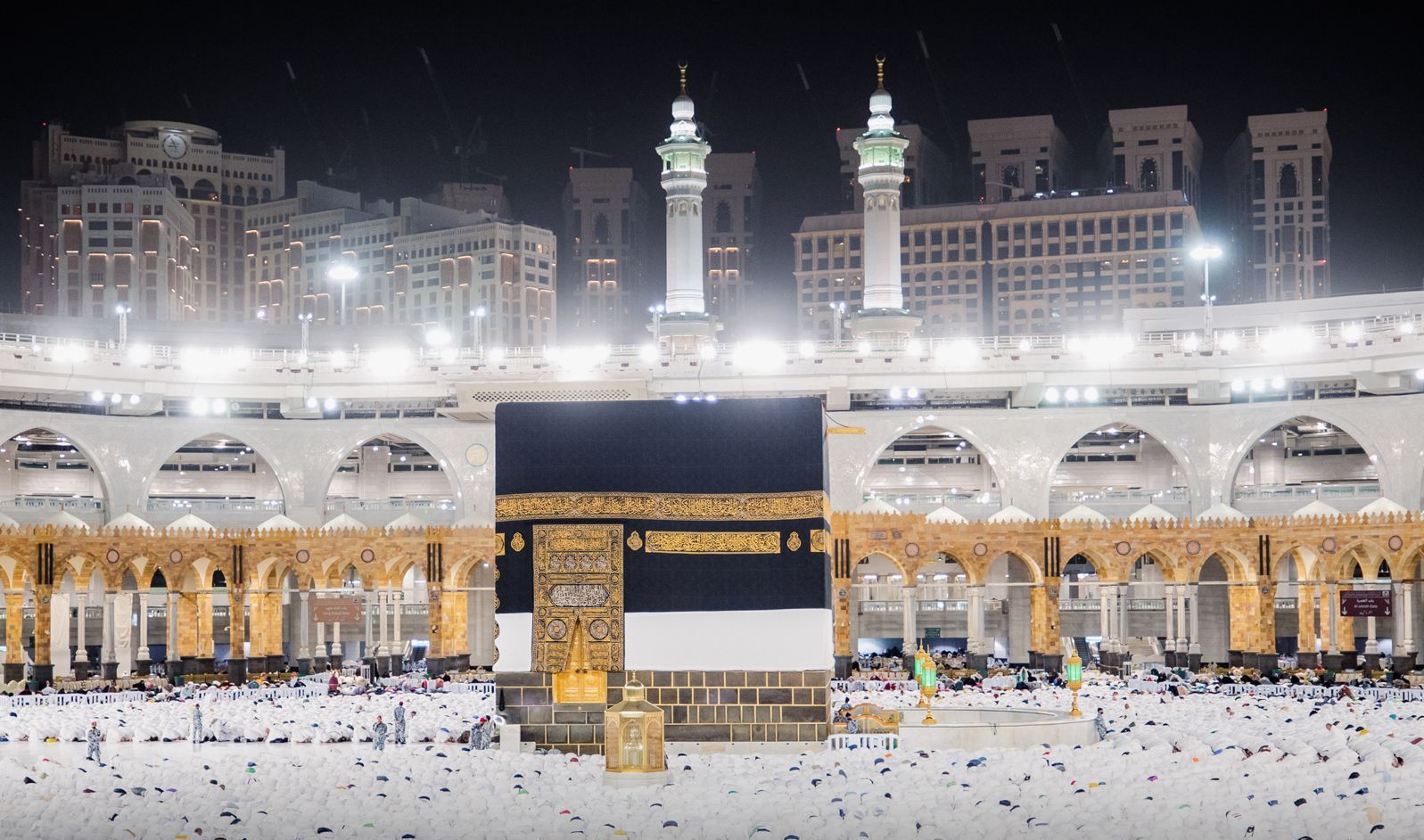 De Kaaba in de Masjid al-Haram in Mekka, 's nachts verlicht en omringd door gelovigen.