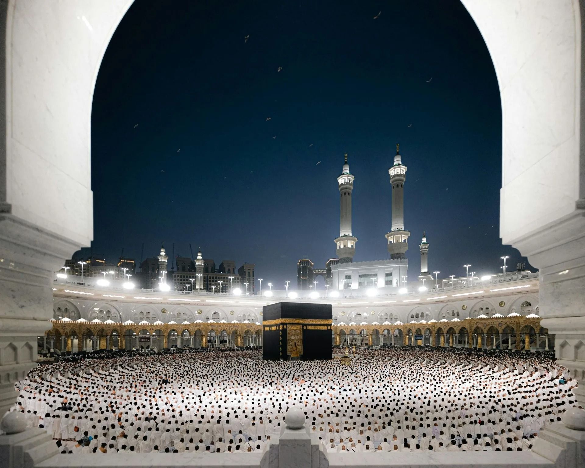 Een menigte pelgrims cirkelt 's nachts rond de Kaaba in Mekka, met op de achtergrond de boog van de Grote Moskee.