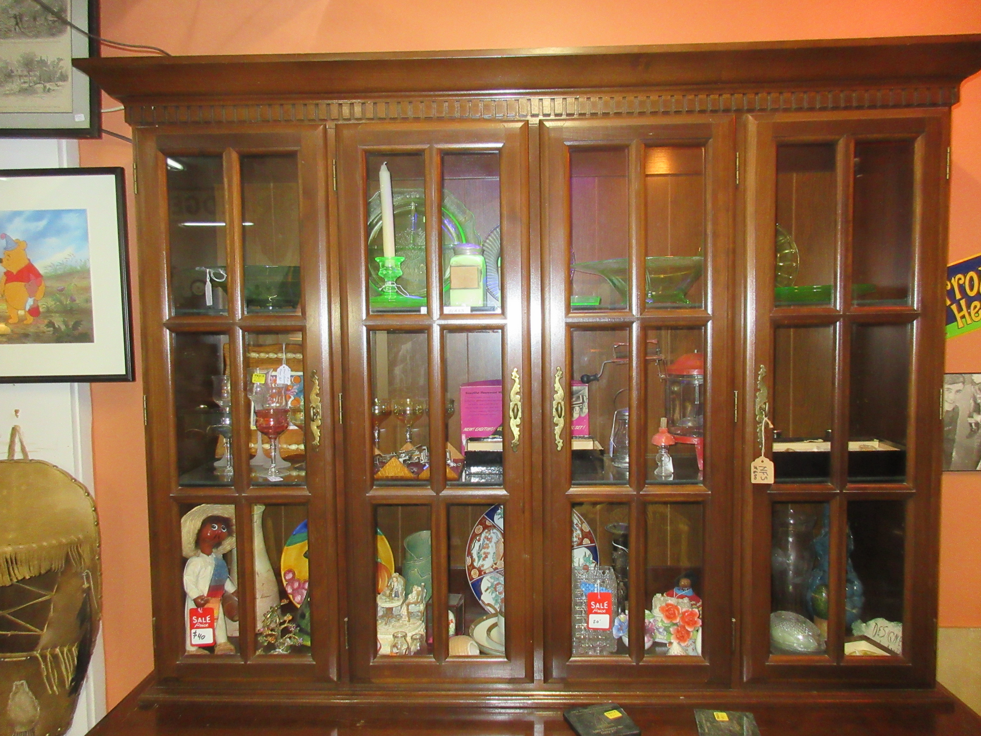 Wooden display cabinet filled with various items, against orange wall.