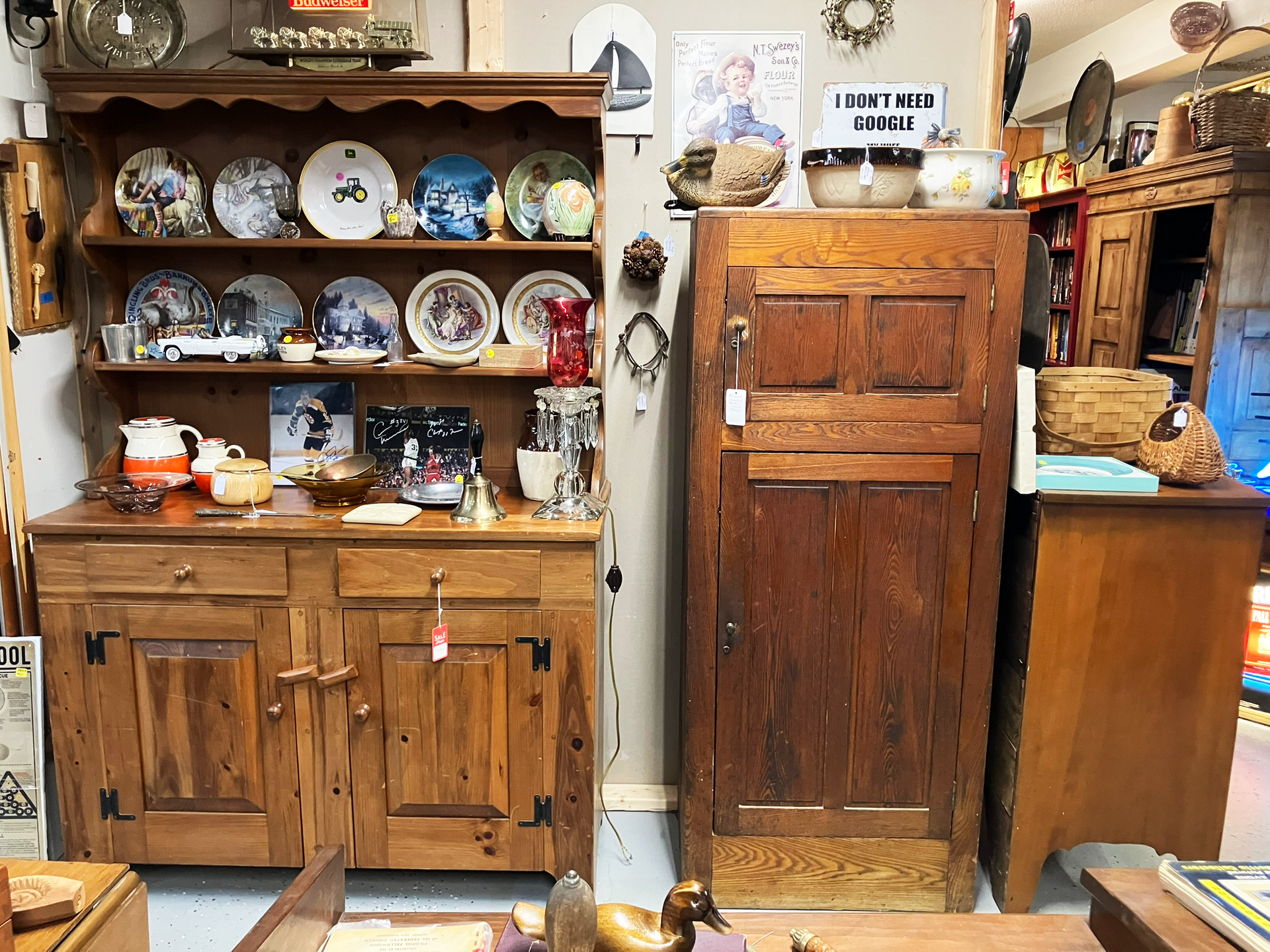 Wooden cabinet and hutch filled with plates and decorative items in a cluttered antique store.