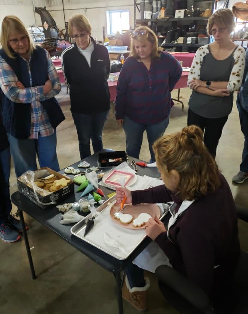A group of women are standing around a table with a plate of food on it