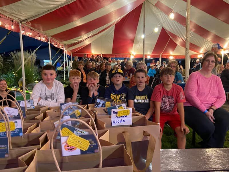 A group of people are sitting under a tent with bags of food.