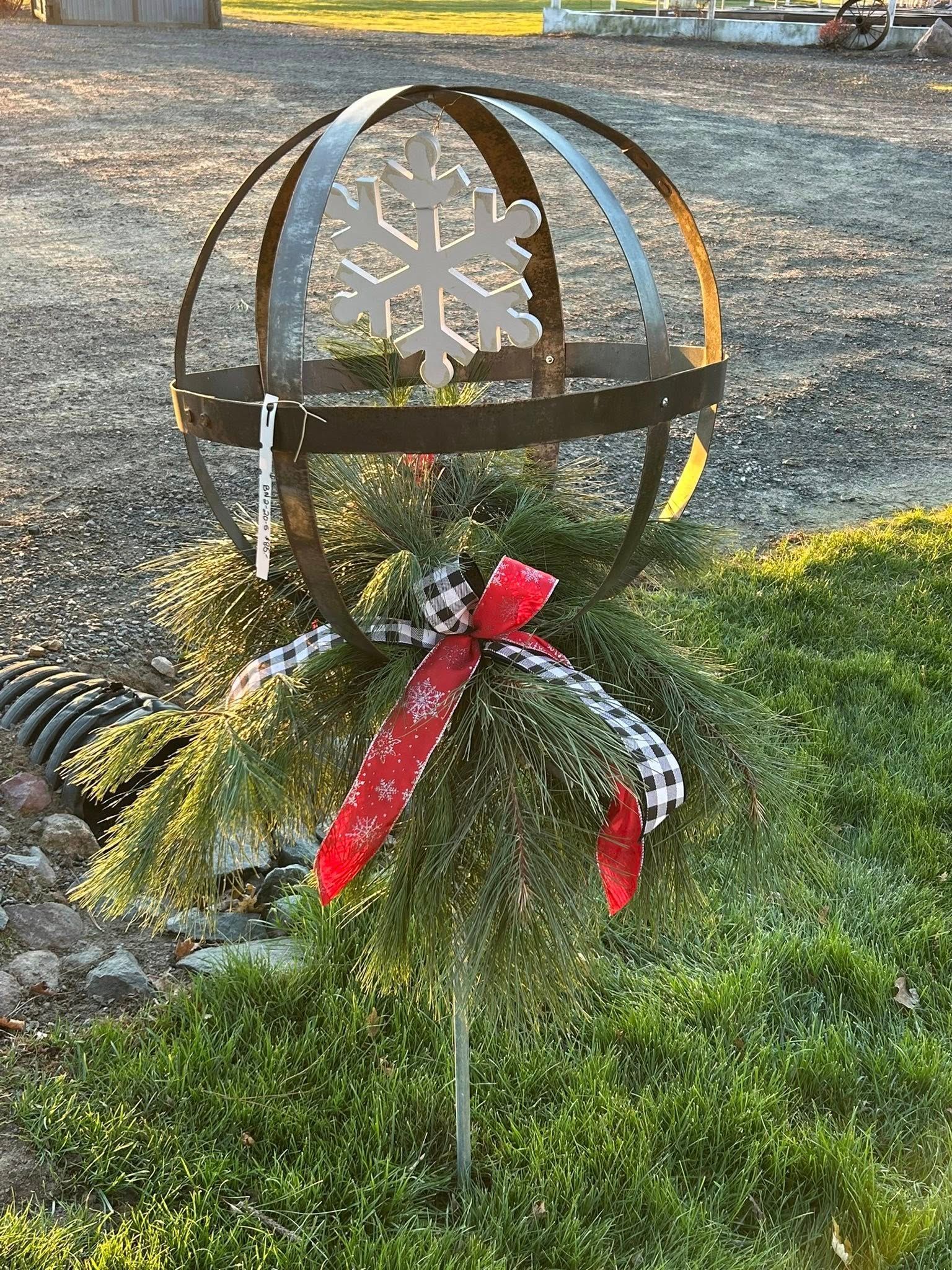Metal sphere garden ornament with a snowflake, greenery, and red bow.