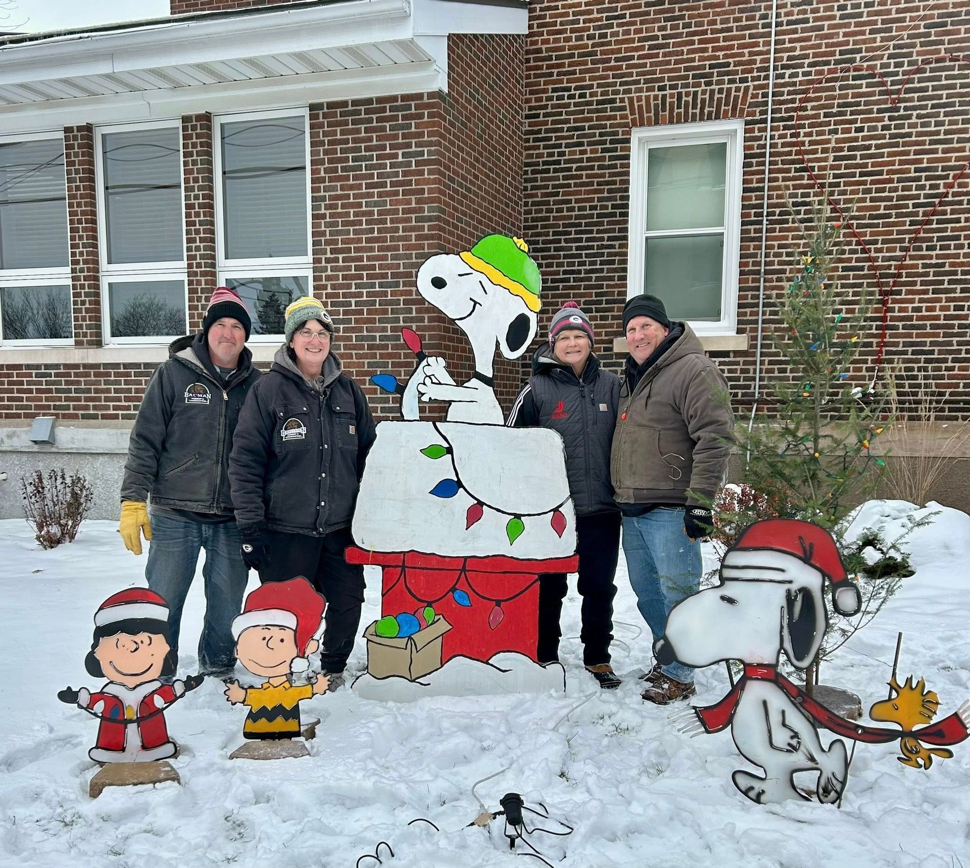 Group of five people with Snoopy and Charlie Brown Christmas decorations in the snow.