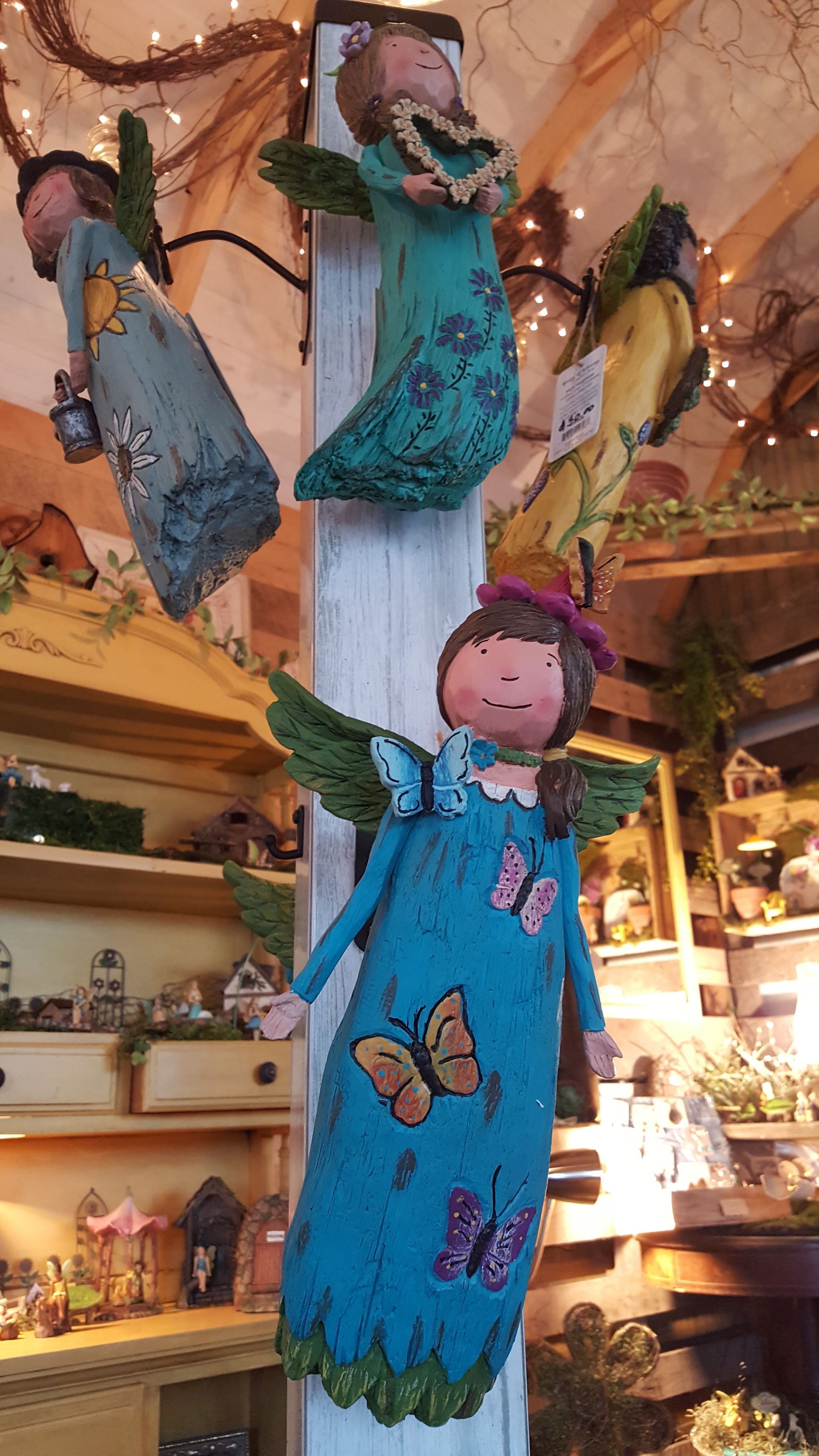Angels with wings and dresses hanging in a shop, some with butterflies.
