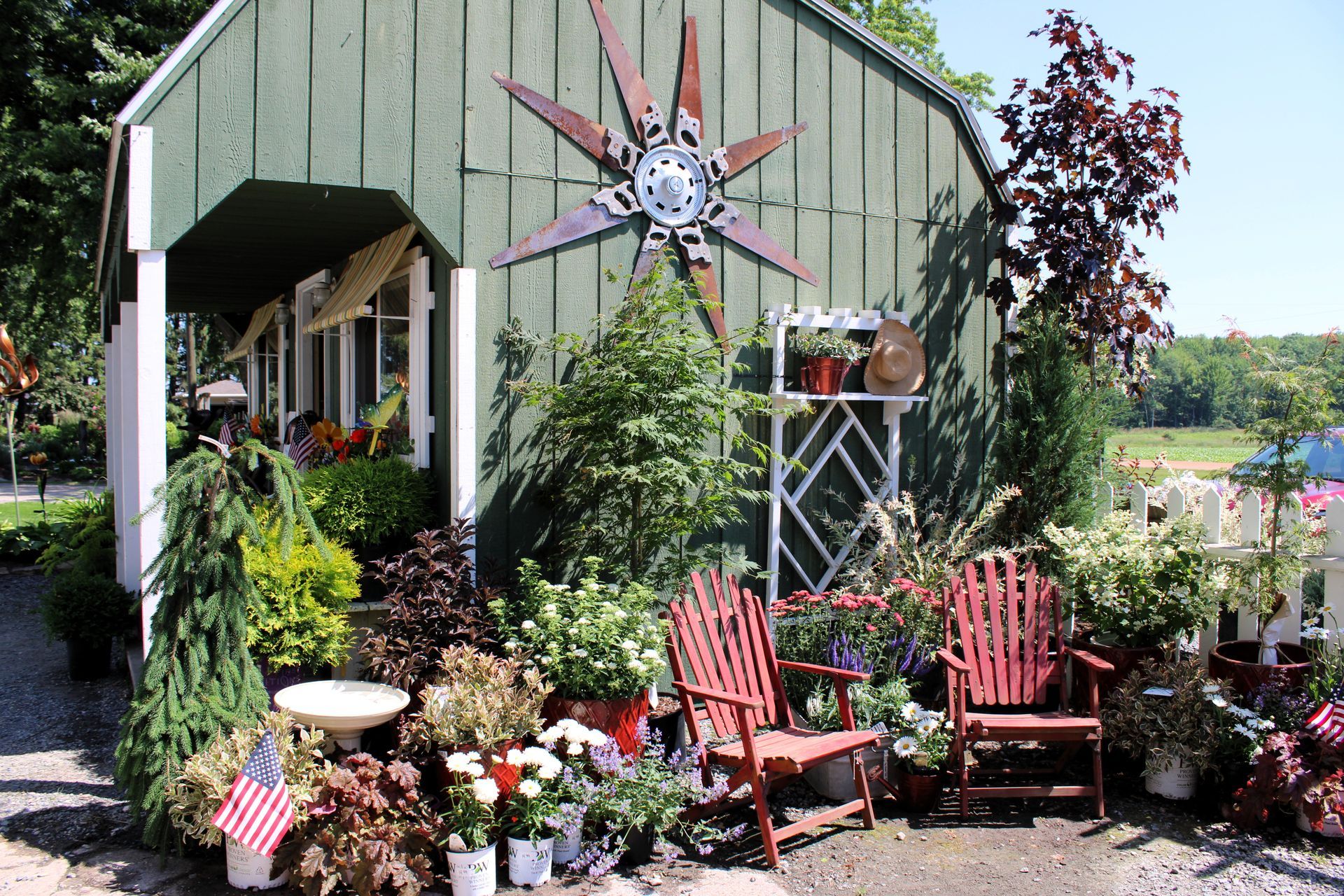 Green building with red Adirondack chairs, surrounded by plants and flowers at a garden center.